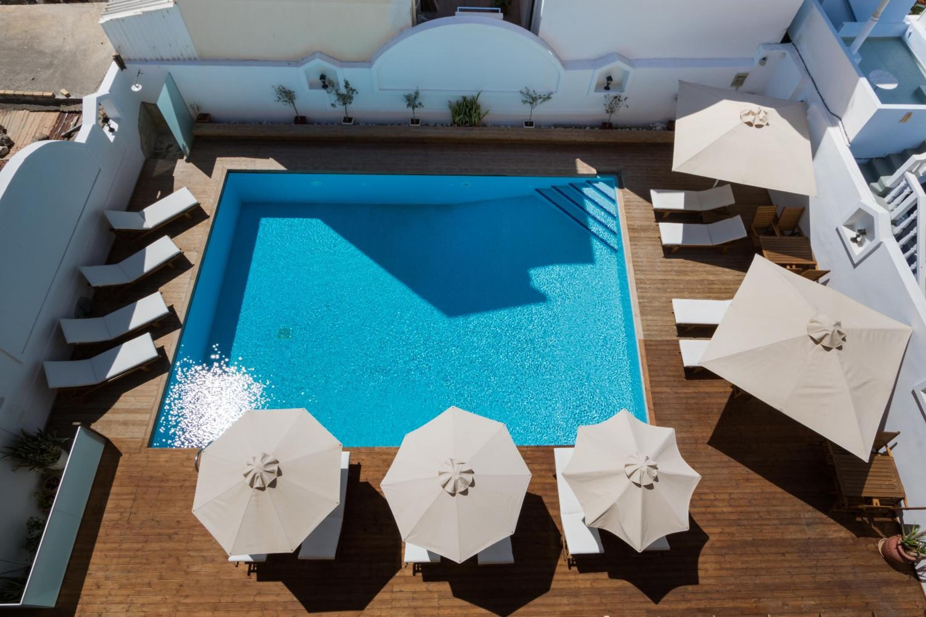 Una piscina en la azotea con terraza de madera, rodeada de sillones blancos y sombrillas.