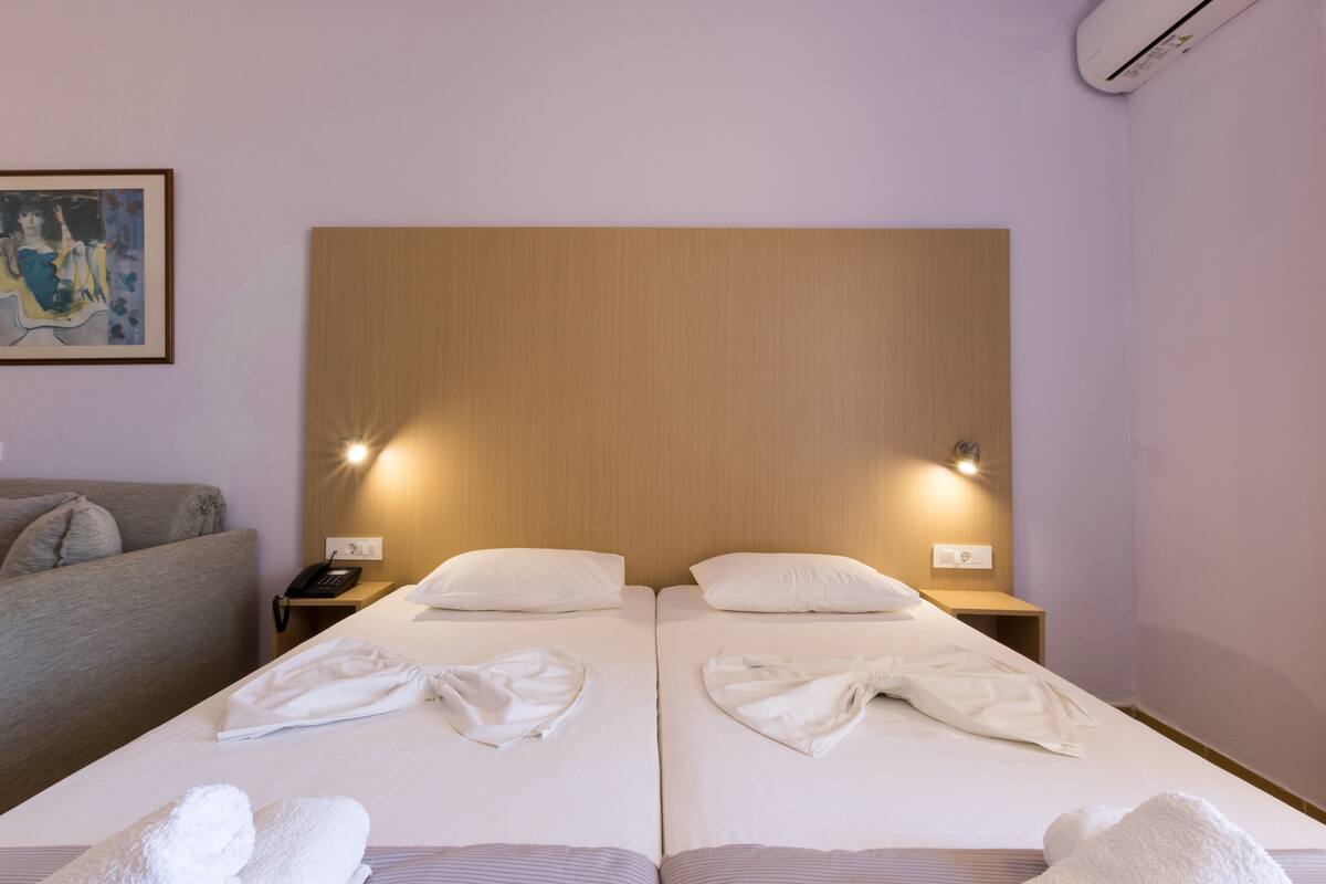 A hotel room with two beds, a bedside table with a phone, and a painting on the wall.