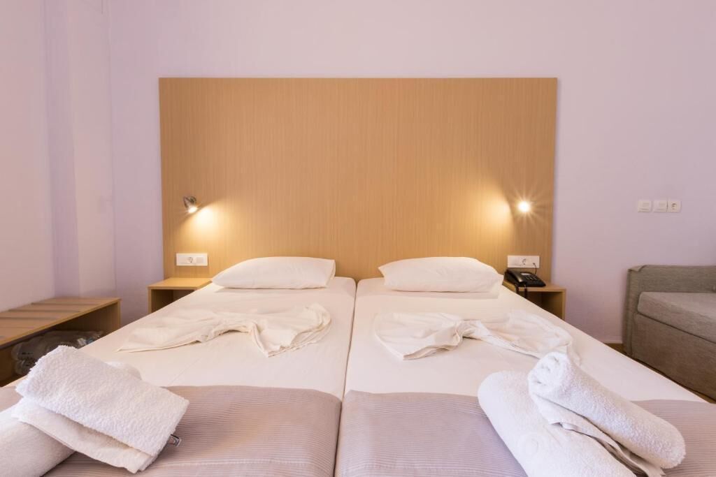 A double room with two beds, each with a wooden headboard, white linens, and a bedside table with a lamp.