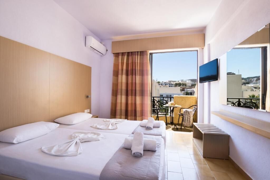 A hotel room with a bed, a TV, a balcony with a table and chairs, and a city view.