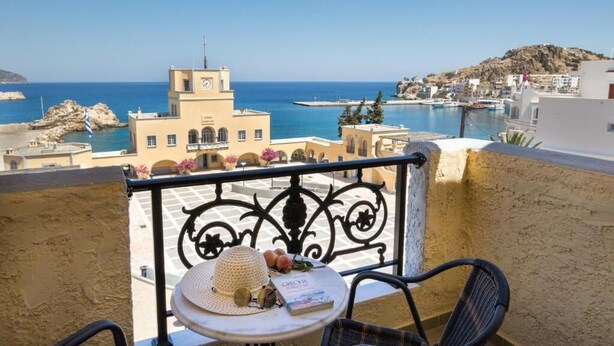 A balcony with a view of the sea, a table with a hat and book, and a chair. - Atlantis Hotel (Karpathos)