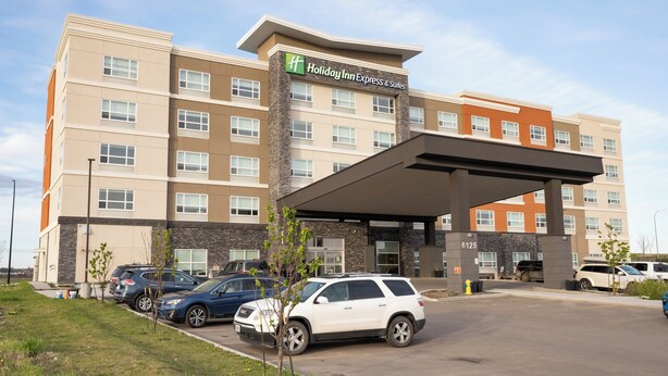 Een Holiday Inn Express & Suites gebouw met een overdekte entree, parkeerplaats en verschillende geparkeerde auto's.