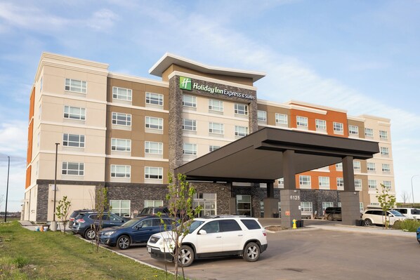Een Holiday Inn Express & Suites gebouw met een overdekte entree, parkeerplaats en verschillende geparkeerde auto's.