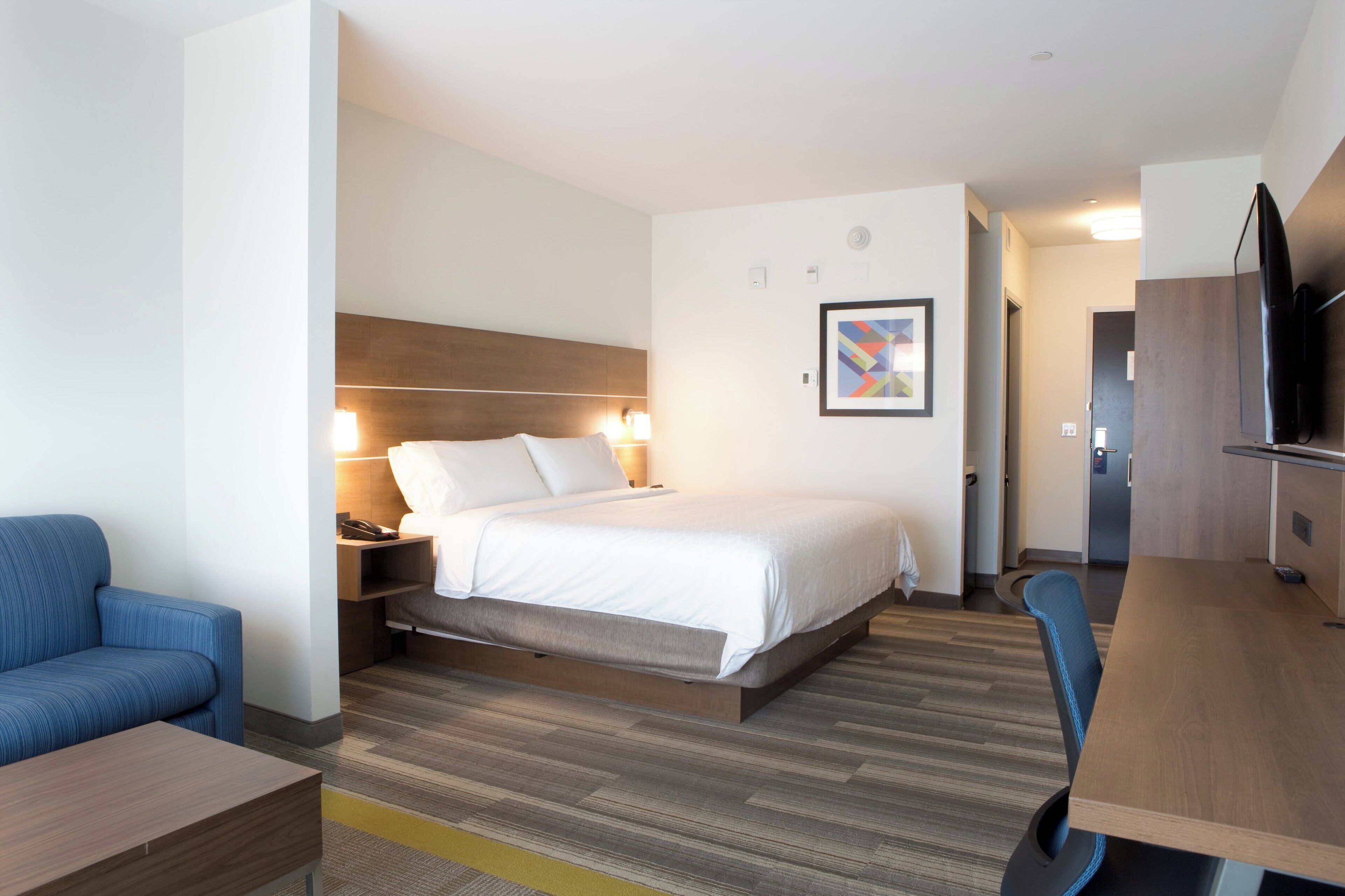 A modern hotel room with a large bed, bedside tables, a desk, a chair, and a TV.