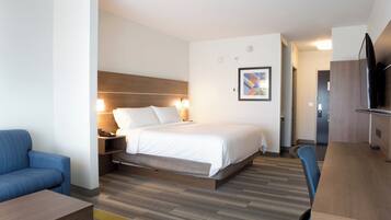A modern hotel room with a large bed, bedside tables, a desk, a chair, and a TV.