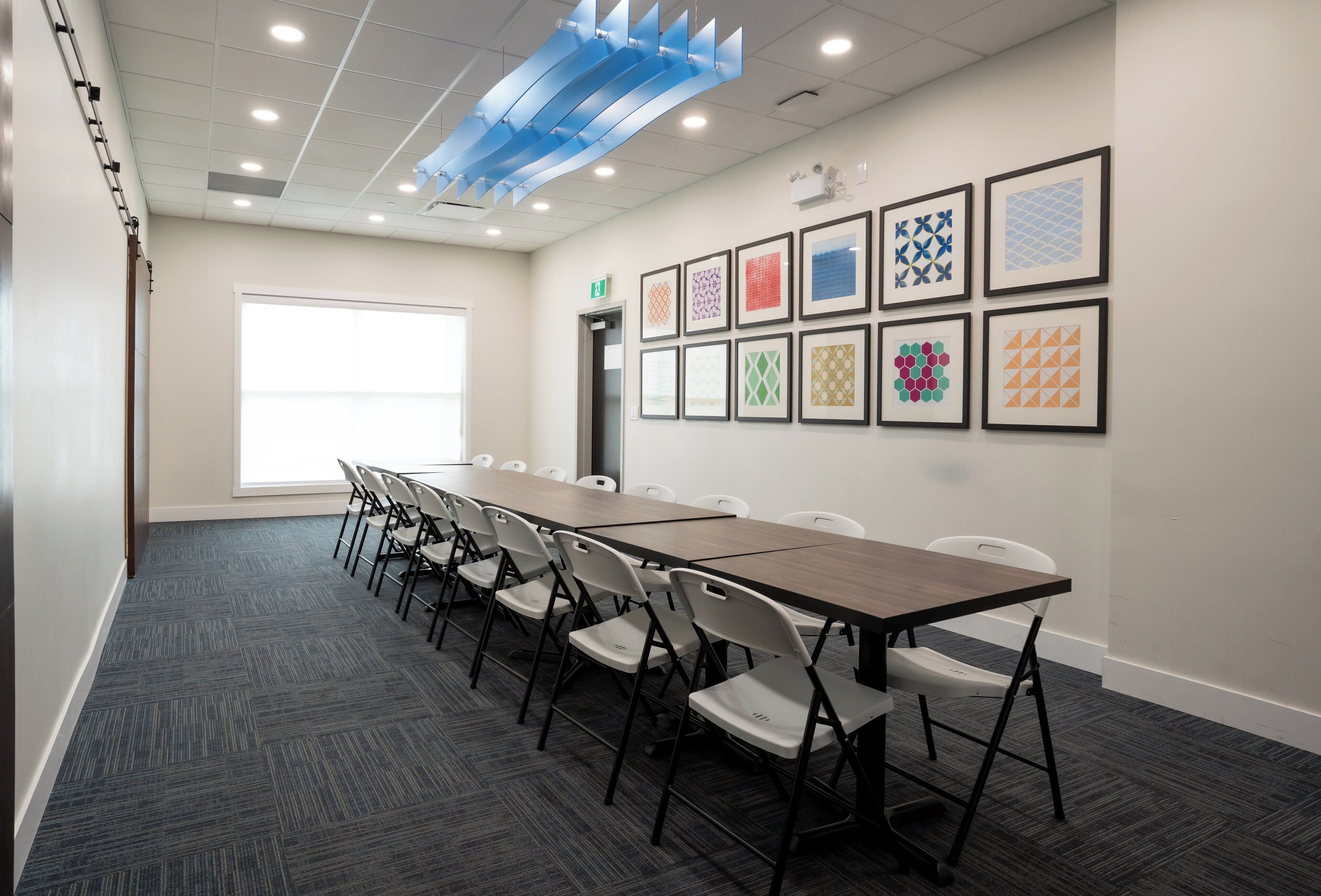 A conference room with a long table, white chairs, and framed wall art.