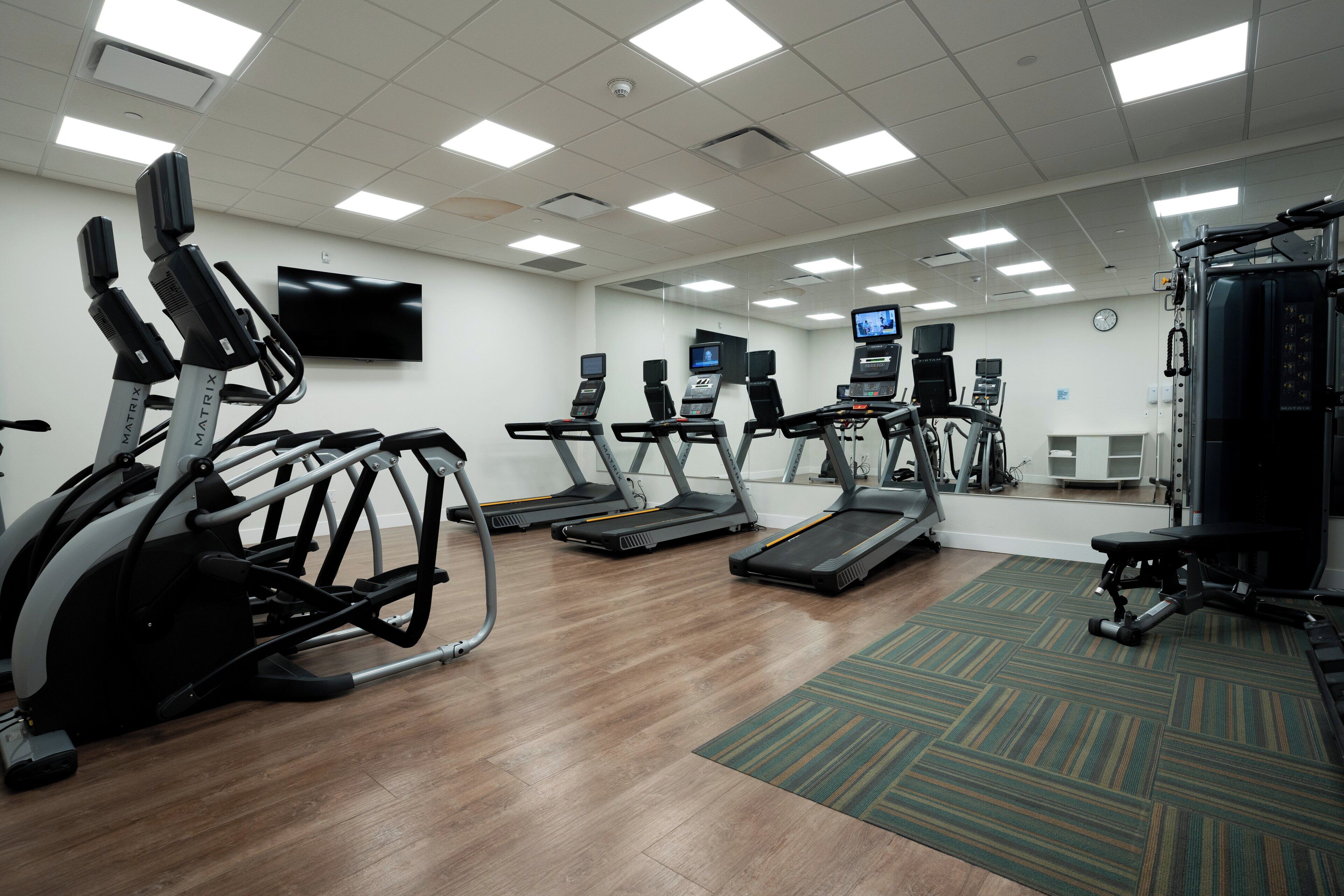 A gym with treadmills, elliptical machines, and a weight bench.