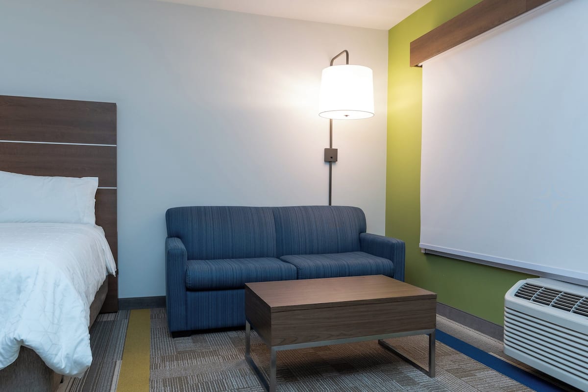 Une chambre d’hôtel avec un lit, un canapé bleu, une table en bois, une lampe fixée au mur et un appareil de climatisation.