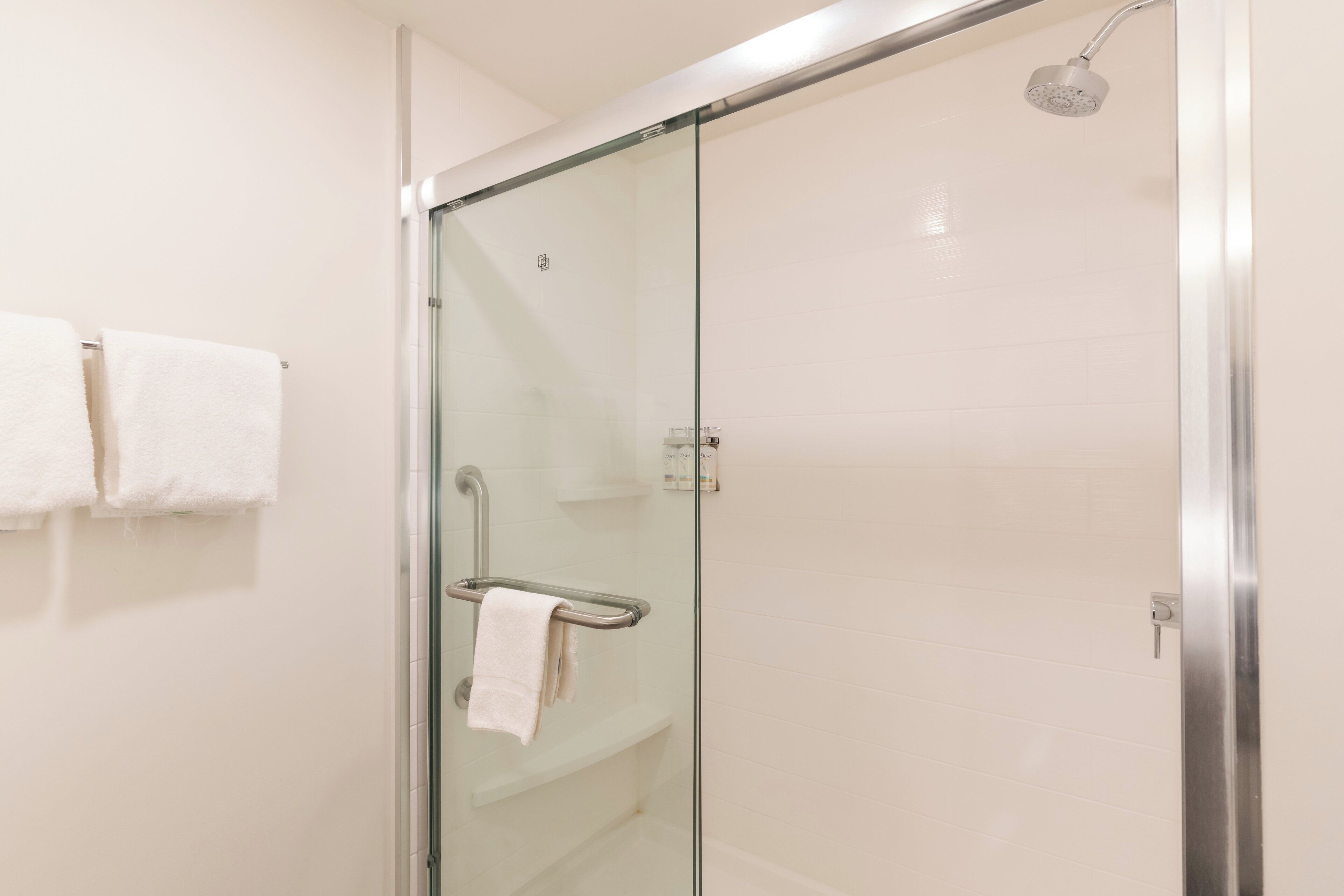 Ducha con paredes de vidrio, cabezal de ducha de mano, toallero con dos toallas y panel de control en la pared.