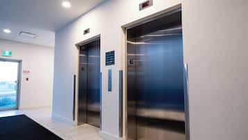 An elevator area with two elevators, a fire exit sign, and a control panel.