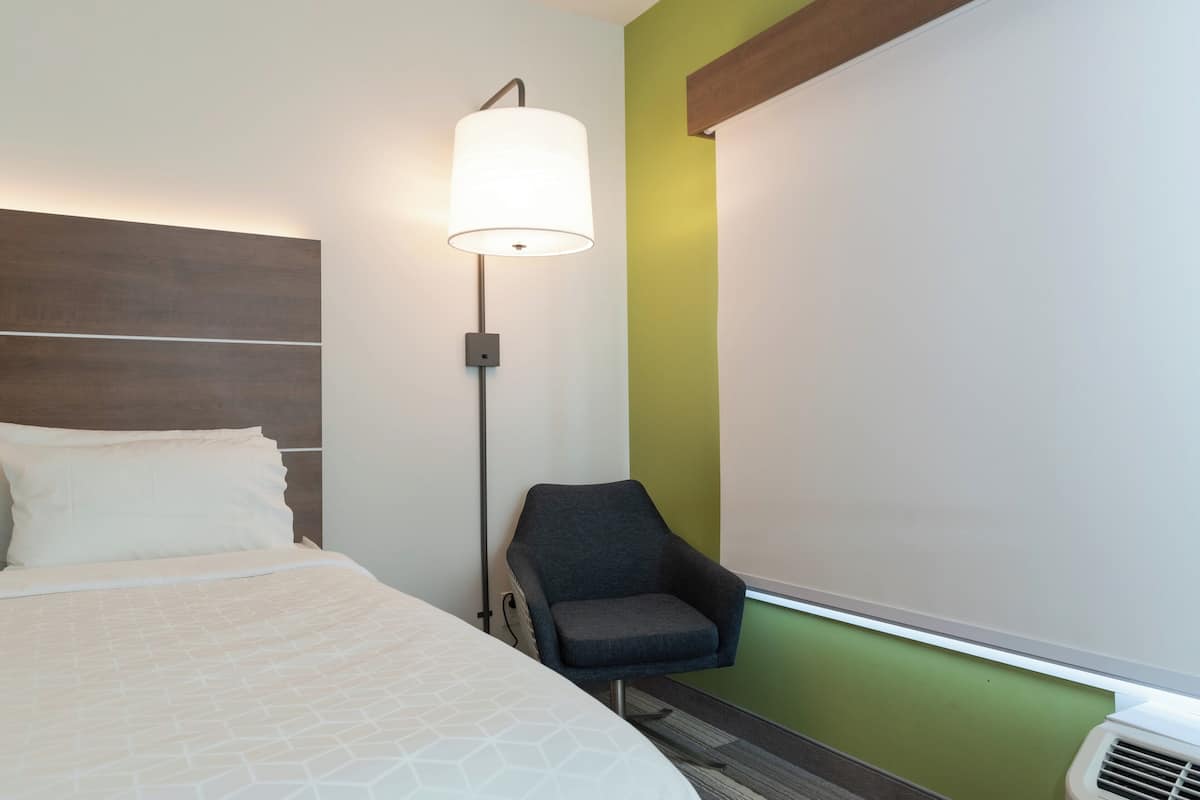 Une chambre d’hôtel avec un lit, une chaise, un lampadaire et un mur agrémenté d’une touche de couleur verte.