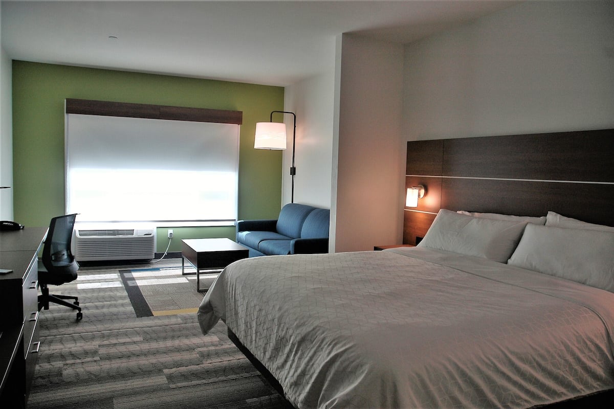 Une chambre d’hôtel avec un grand lit, un bureau, une chaise, un canapé et une fenêtre avec des stores.