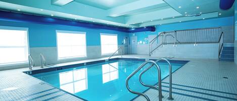 Une piscine intérieure avec des marquages bien visibles, un sol carrelé et un escalier menant à un niveau supérieur.