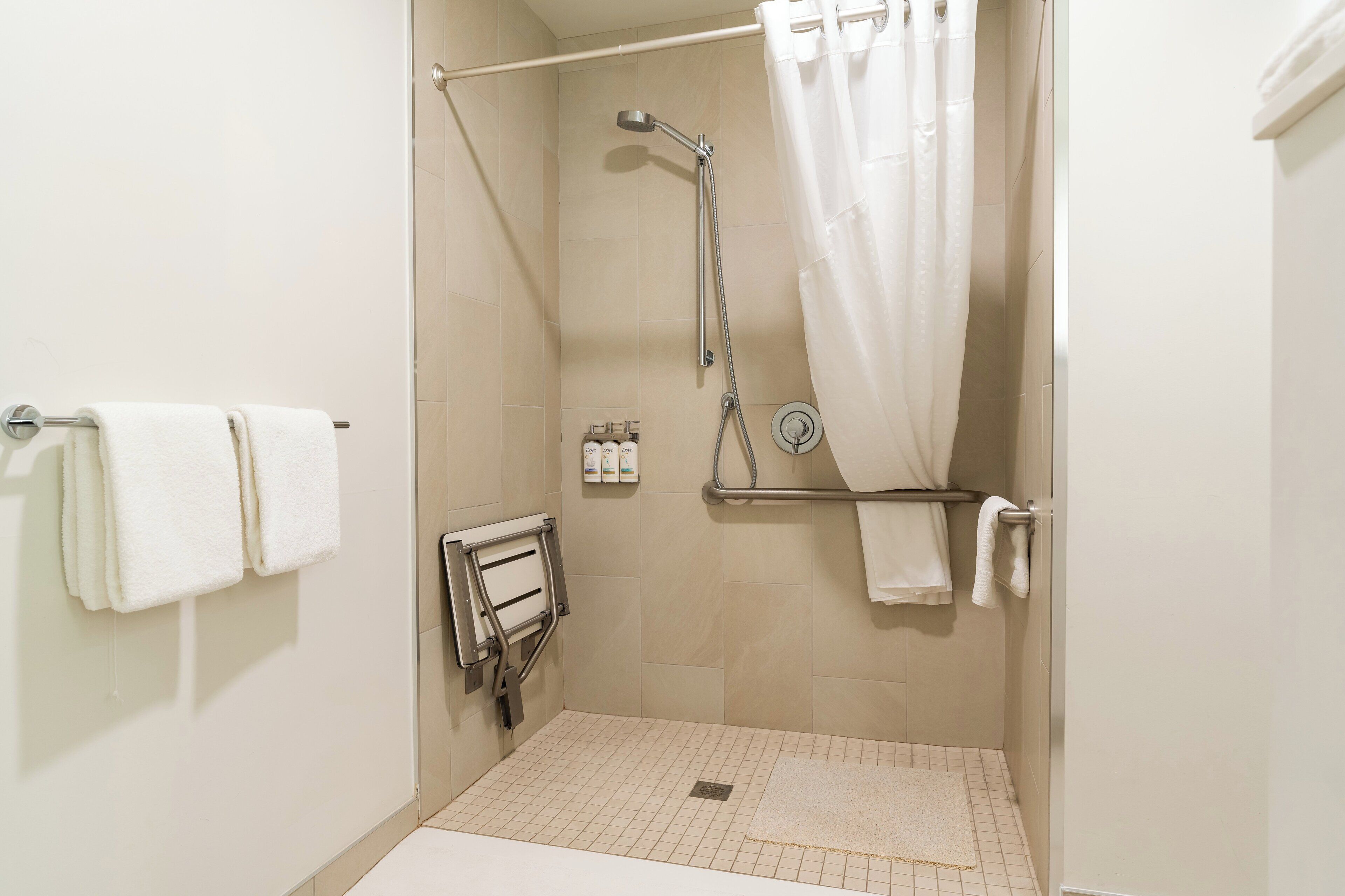 A walk-in shower with a grab bar, a white towel rack, and a shower curtain.