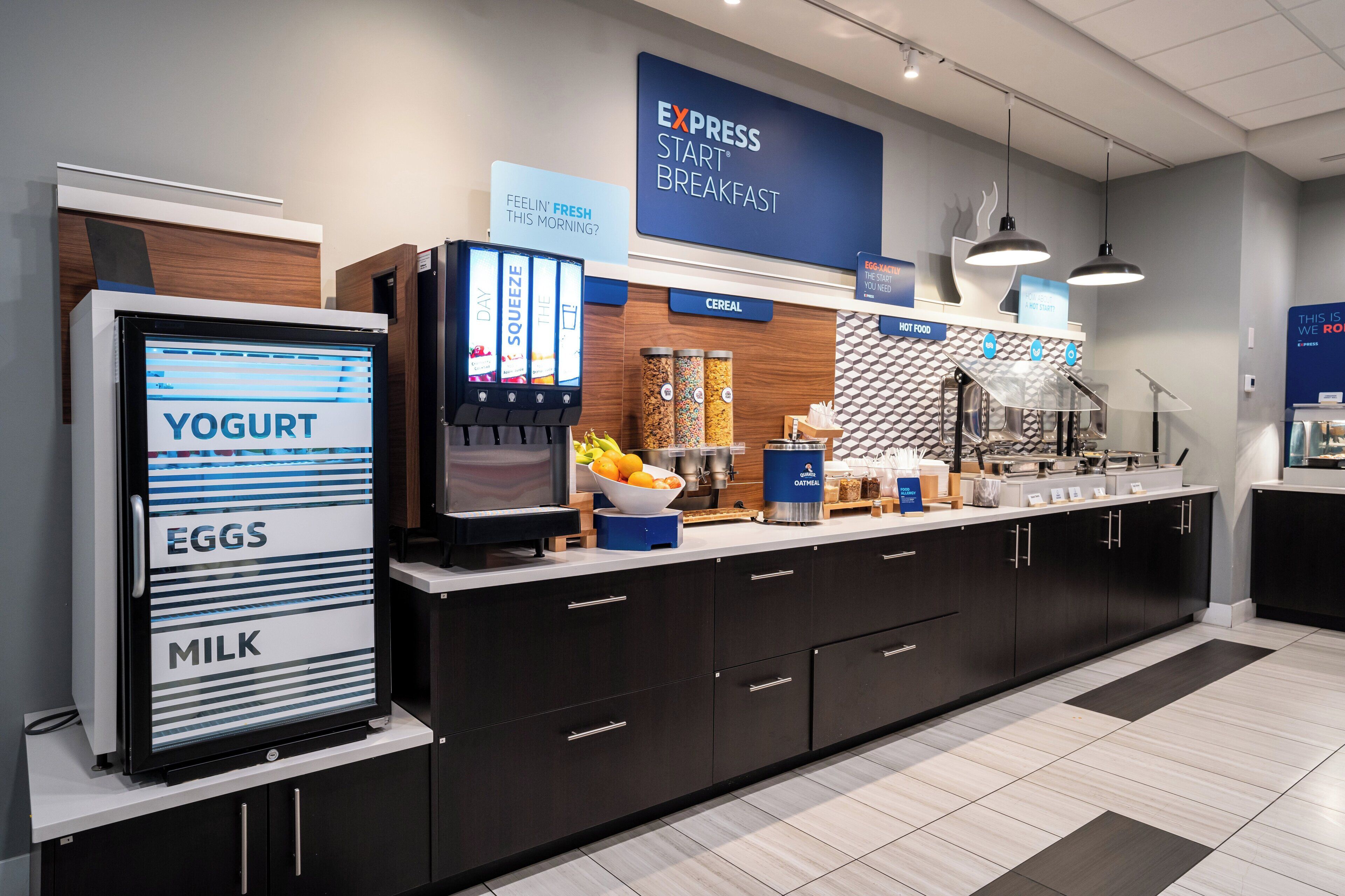 A modern breakfast bar with a digital menu display, yogurt, eggs, and milk dispensers, and a variety of hot food options.