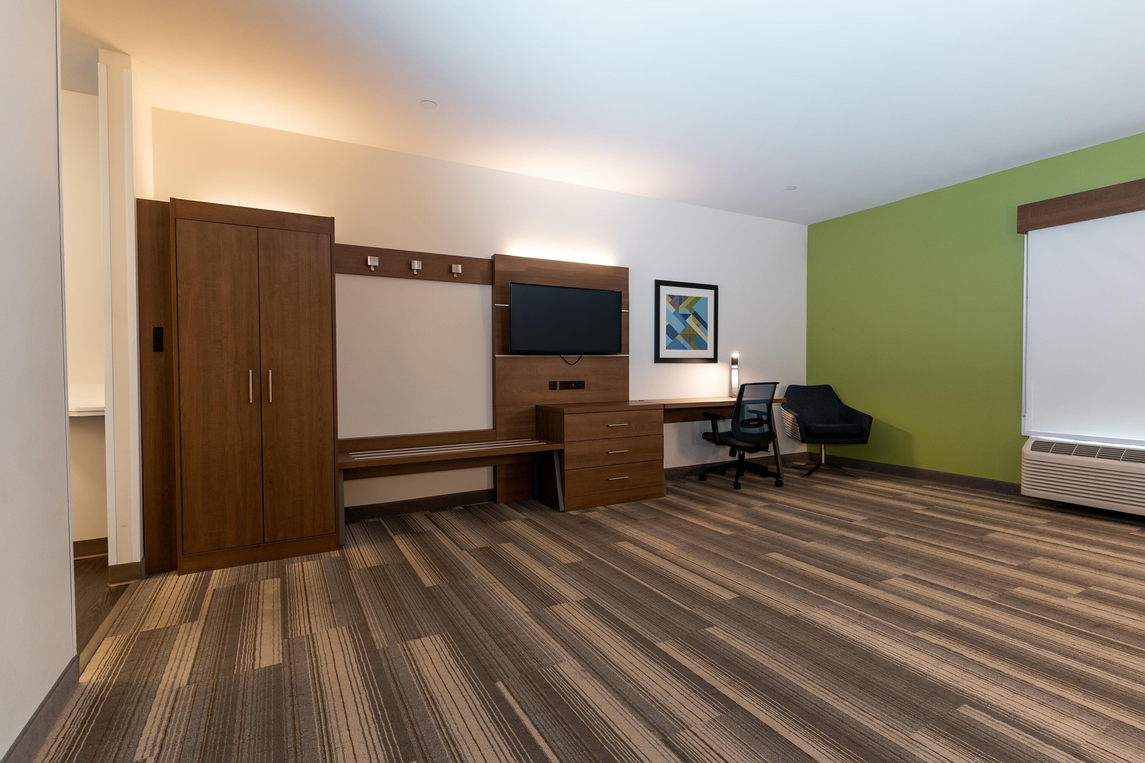 Une chambre d’hôtel avec une armoire en bois, un bureau doté d’un téléviseur à écran plat, une chaise et un mur d’accent vert.