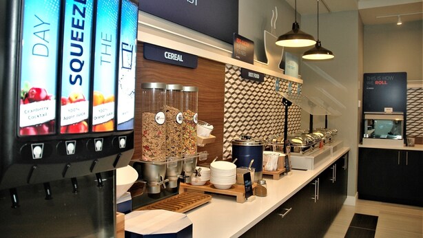 A breakfast buffet area with labeled drink dispensers, a cereal section, and a variety of hot foods. - Holiday Inn Express & Suites Edmonton SW - Windermere by IHG (Edmonton)