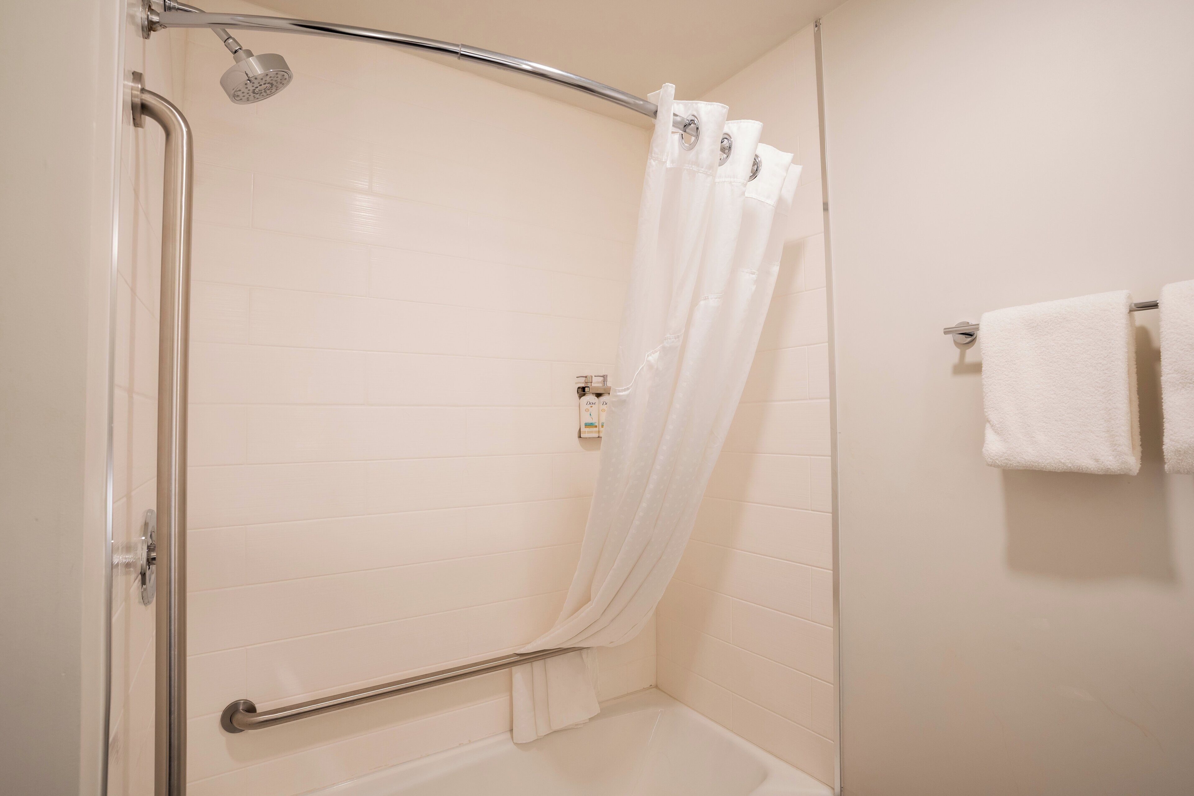 Ducha con puerta de vidrio, cortina de ducha blanca y pasamanos.
