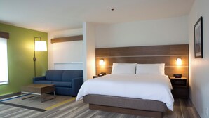 Een hotelkamer met een groot bed, een bank, een nachtkastje met lamp en een wandlamp.