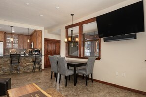 A modern kitchen with wooden cabinets, a stone backsplash, and a dining area with a table and chairs.