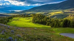 A golf course with a pond, surrounded by forested hills.