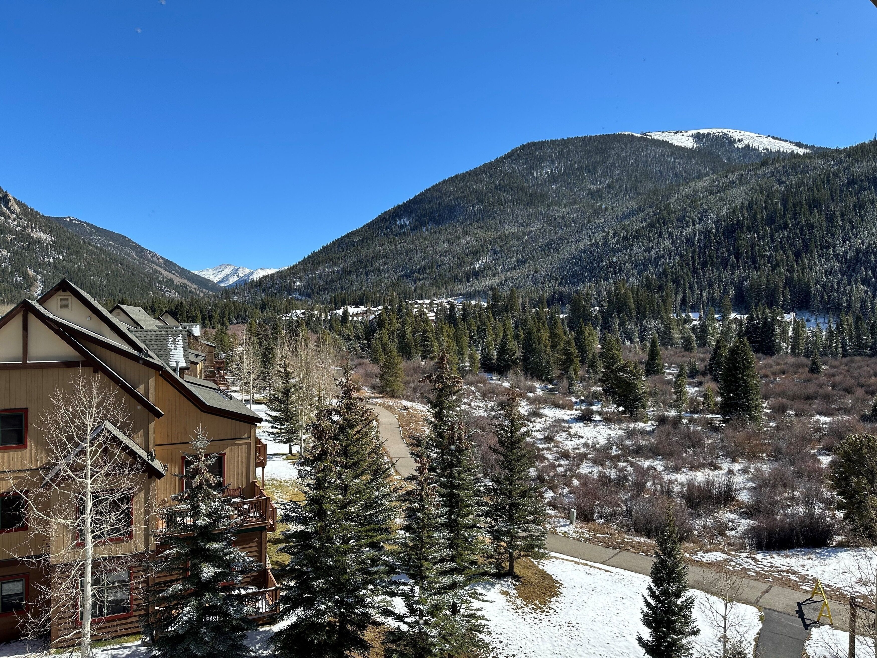 Eine Berglodge mit Holzbauten, einer Terrasse und Blick auf schneebedeckte Berge.