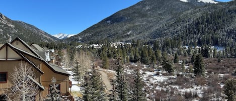 A mountain lodge with a wooden exterior, a deck, and a view of snow-covered mountains.