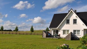 Een huis met een groot gazon, een houten omheining en een heldere lucht.