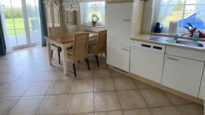 Een ruime keuken met een eettafel, stoelen, een kroonluchter en uitzicht op het groen.
