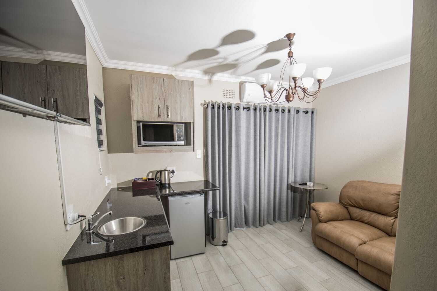 A compact kitchen with a microwave, coffee maker, and a small refrigerator. There's a sofa and a small table in the living area.