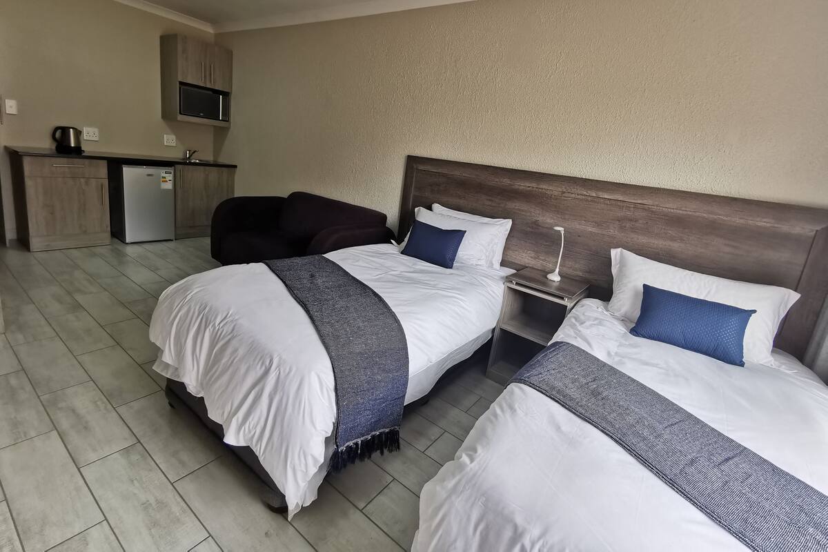 Habitación de hotel con dos camas, una kitchenette pequeña y un cabecero de madera.