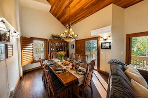 A dining area with a wooden table, chairs, a chandelier, and a view through the window. - 1687 Lakeside 3 Bedroom Home by RedAwning (Park City)