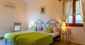 Un dormitorio con dos camas, un radiador, aire acondicionado, una ventana con cortinas y un cuadro en la pared.