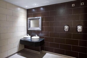 A modern bathroom with two sinks, a large mirror, and a dark tiled wall. - Furness Railway by Wetherspoon (Barrow-in-Furness)