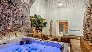 Un baño moderno con pared de piedra, una bañera con múltiples chorros, una planta en maceta y un tocador de madera.