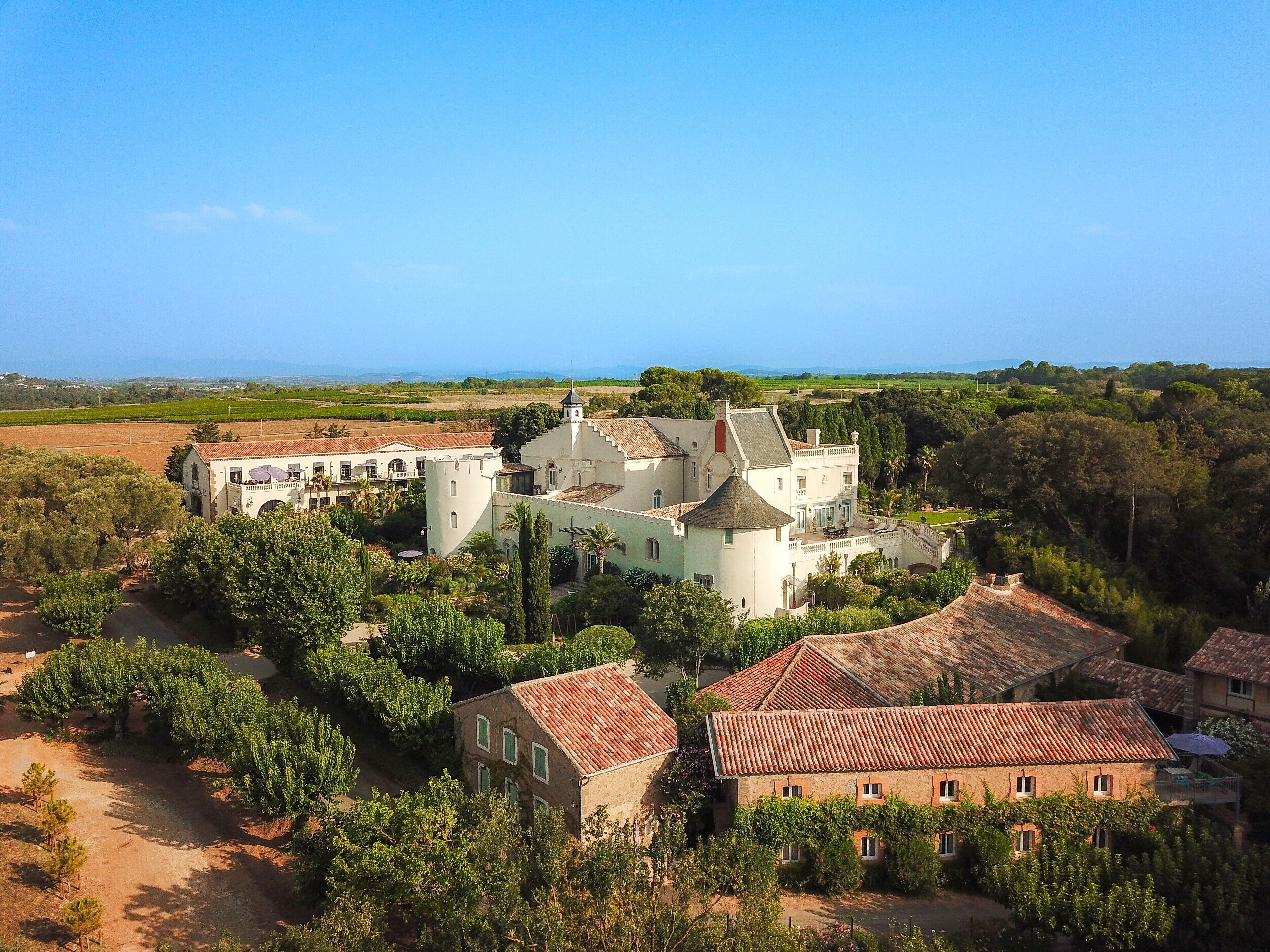 A large white building with a tower, surrounded by trees and smaller buildings with red-tiled roofs.