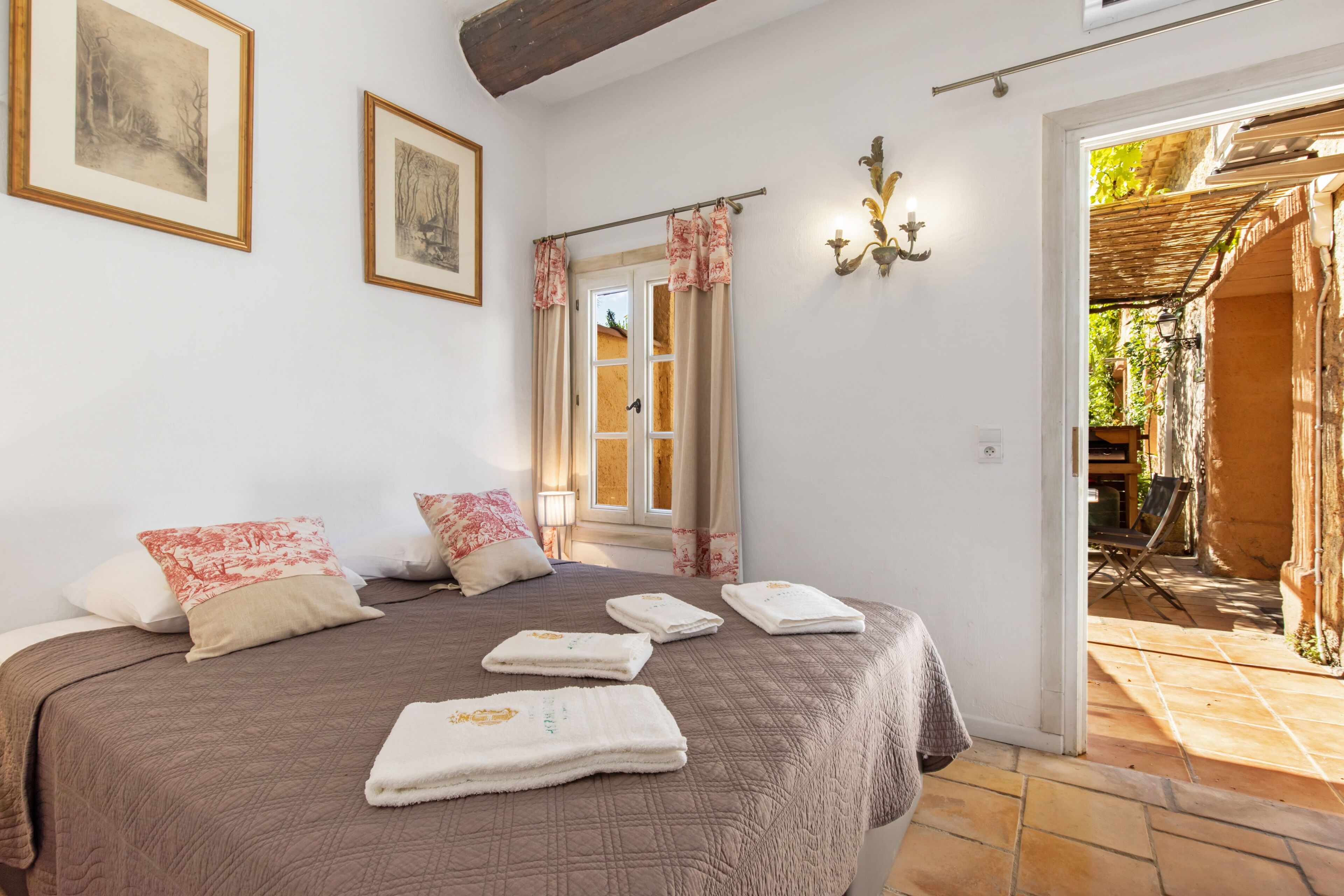 Un dormitorio con una cama grande, dos cuadros enmarcados, una ventana con cortinas y vistas a un espacio exterior.