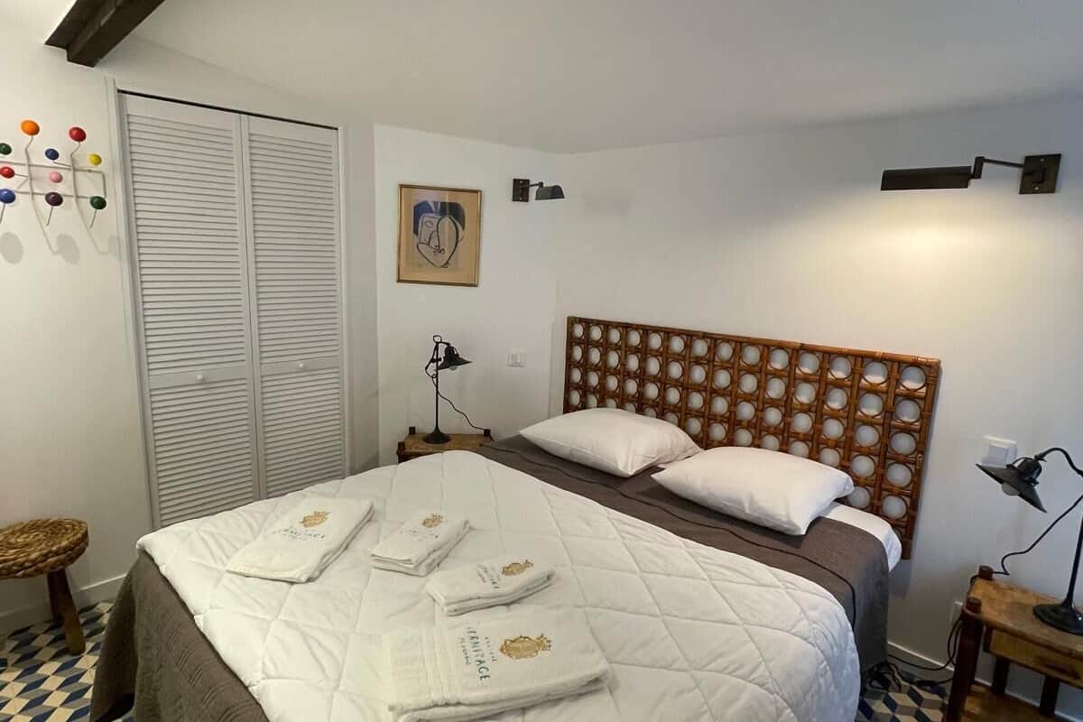 Un dormitorio con una cama grande, un cabecero de madera, una mesita de noche, una lámpara, un estante en la pared y un suelo estampado.