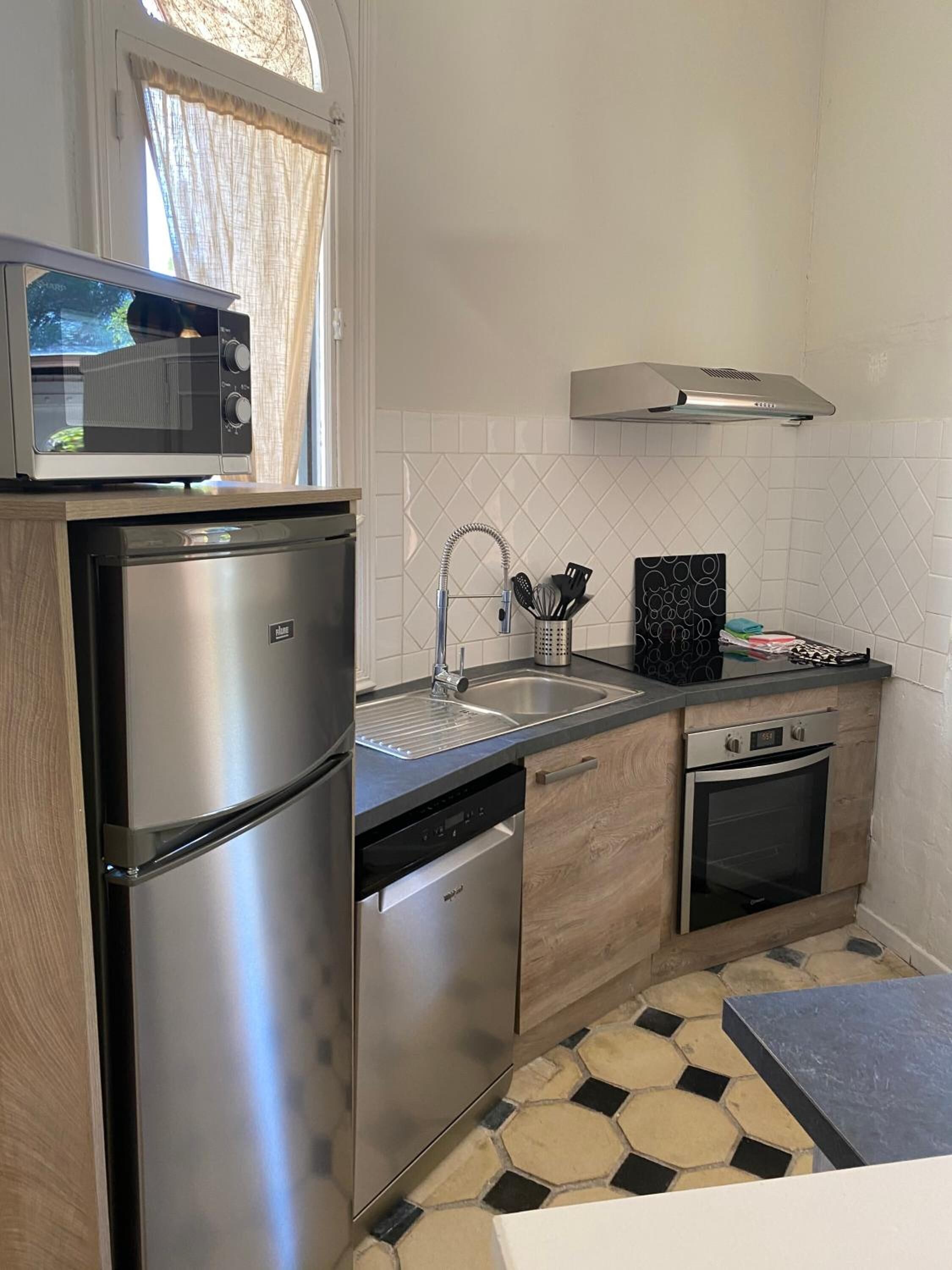 Cocina compacta con electrodomésticos de acero inoxidable, microondas, pileta con grifo, escurreplatos y salpicadero de cerámica.