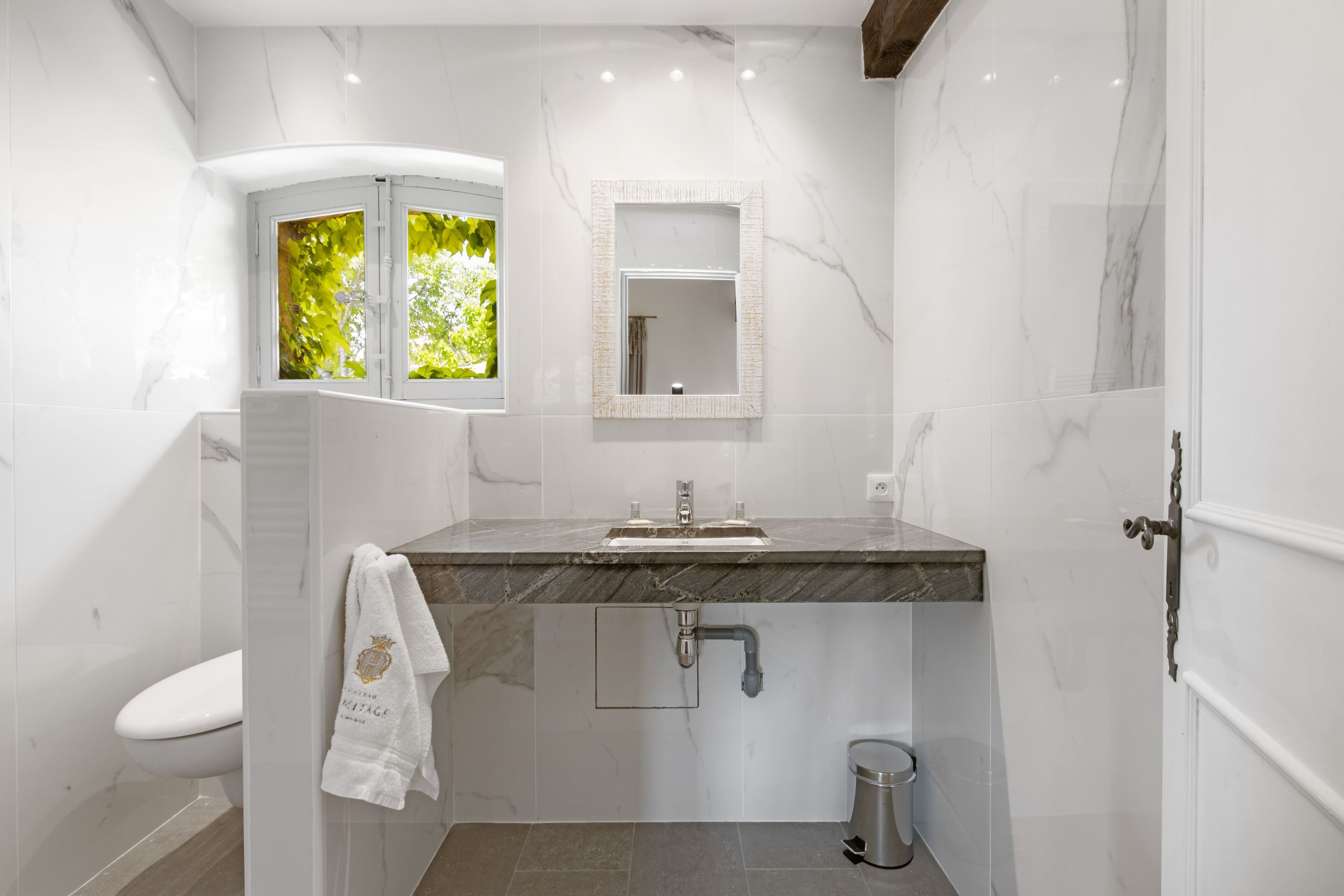 A modern bathroom with a marble vanity, a sink, a mirror, and a toilet.