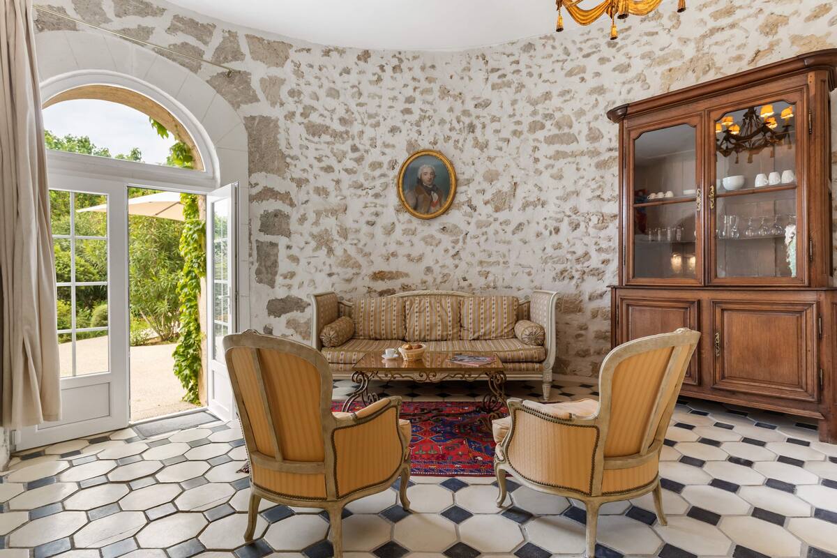 Una habitación con pared de piedra, un sofá, dos sillones, un aparador de madera y un ventanal grande.