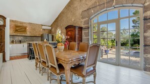 Un comedor con una mesa y sillas de madera, una cocina al fondo y un ventanal con vistas al exterior.