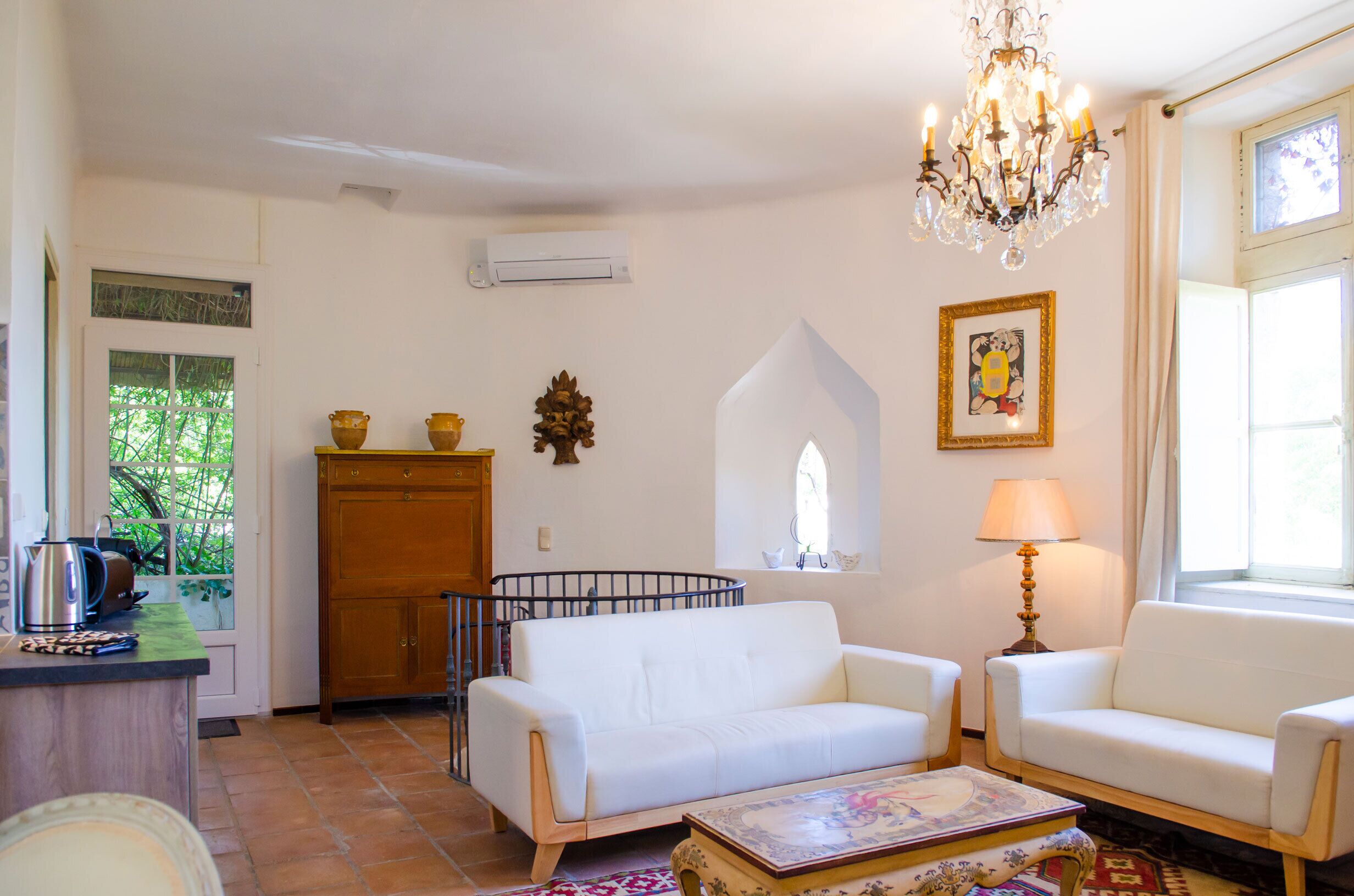 Una sala de estar con un sofá blanco, un mueble de madera, una lámpara de araña y una ventana con cortinas.