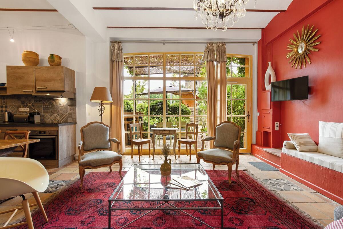 Una sala de estar moderna con una mesa de centro de vidrio, un sofá y un televisor. Se observa una cocina con armarios de madera y una mesa de comedor.