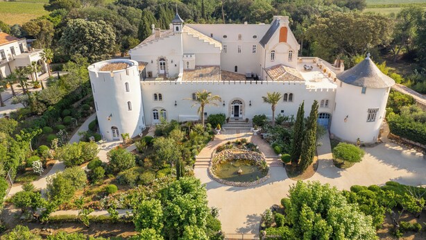 Un edificio grande y blanco, de estilo castillo, con múltiples torres y un patio central con una fuente.