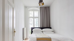 Un dormitorio con cama, ventana con cortinas, radiador y puerta.