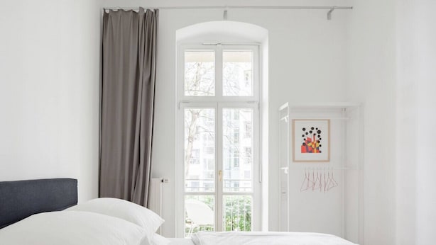Un dormitorio con una cama, una ventana, una puerta con un cuadro enmarcado y una cortina.