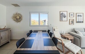 Uma sala de jantar com uma mesa comprida, cadeiras, um sofá e uma janela com vista.