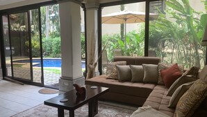 Ein Wohnzimmer mit einer Couch, einem Couchtisch und Blick auf einen Swimmingpool durch große Glasüren.