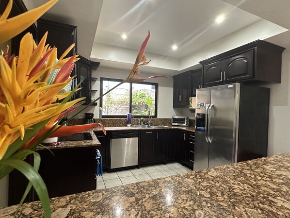 Una cocina moderna con armarios oscuros, un refrigerador de acero inoxidable y una encimera de granito.